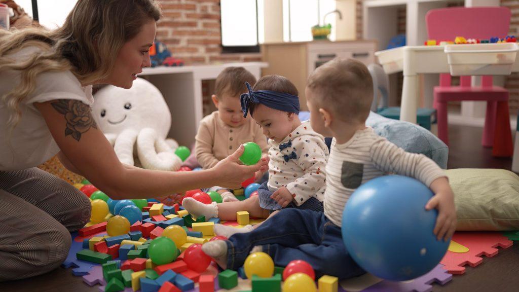 teacher and preschool students playing with balls sitting on floor at kindergarten